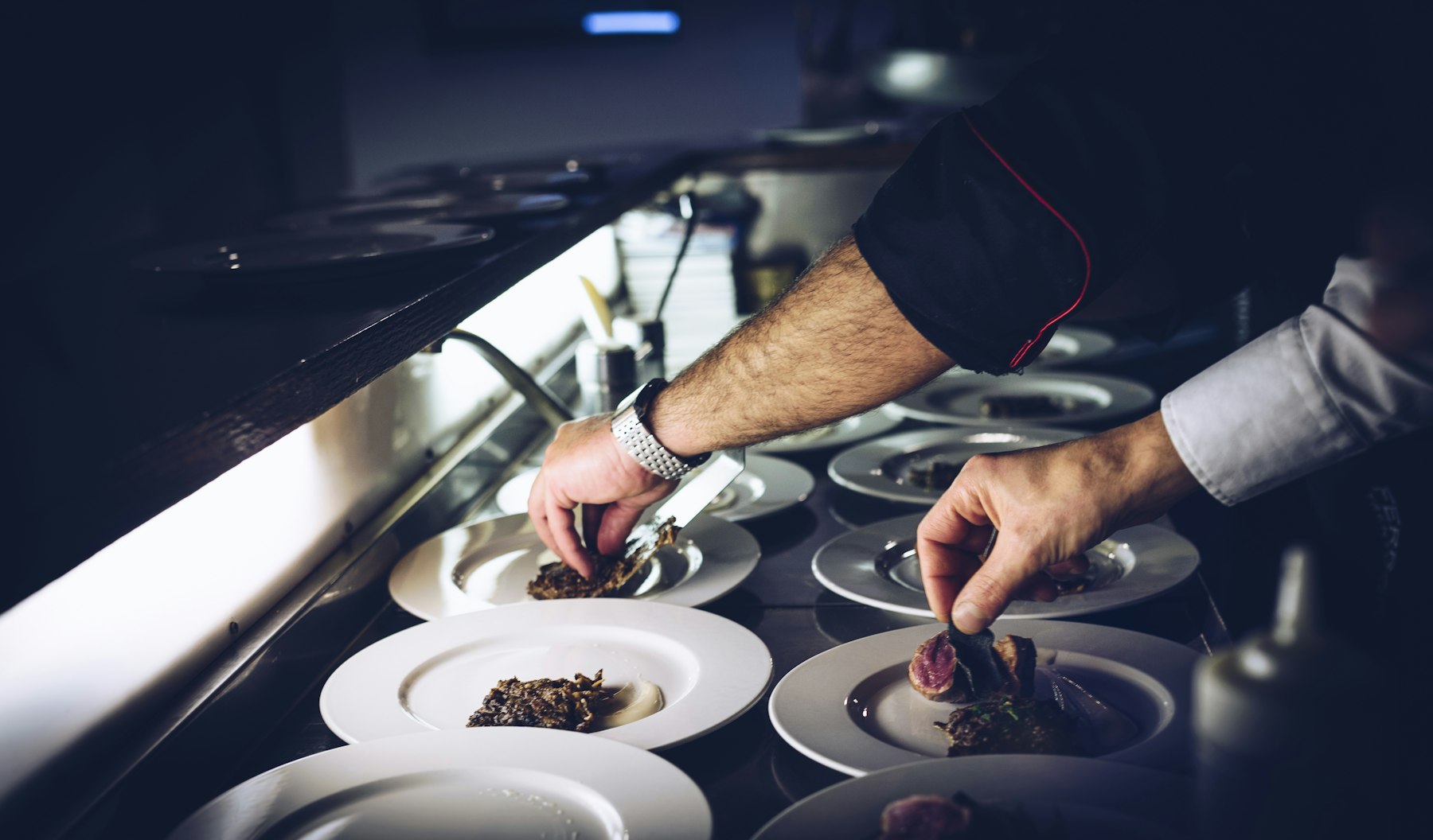 Chef plating a row of dishes at the pass